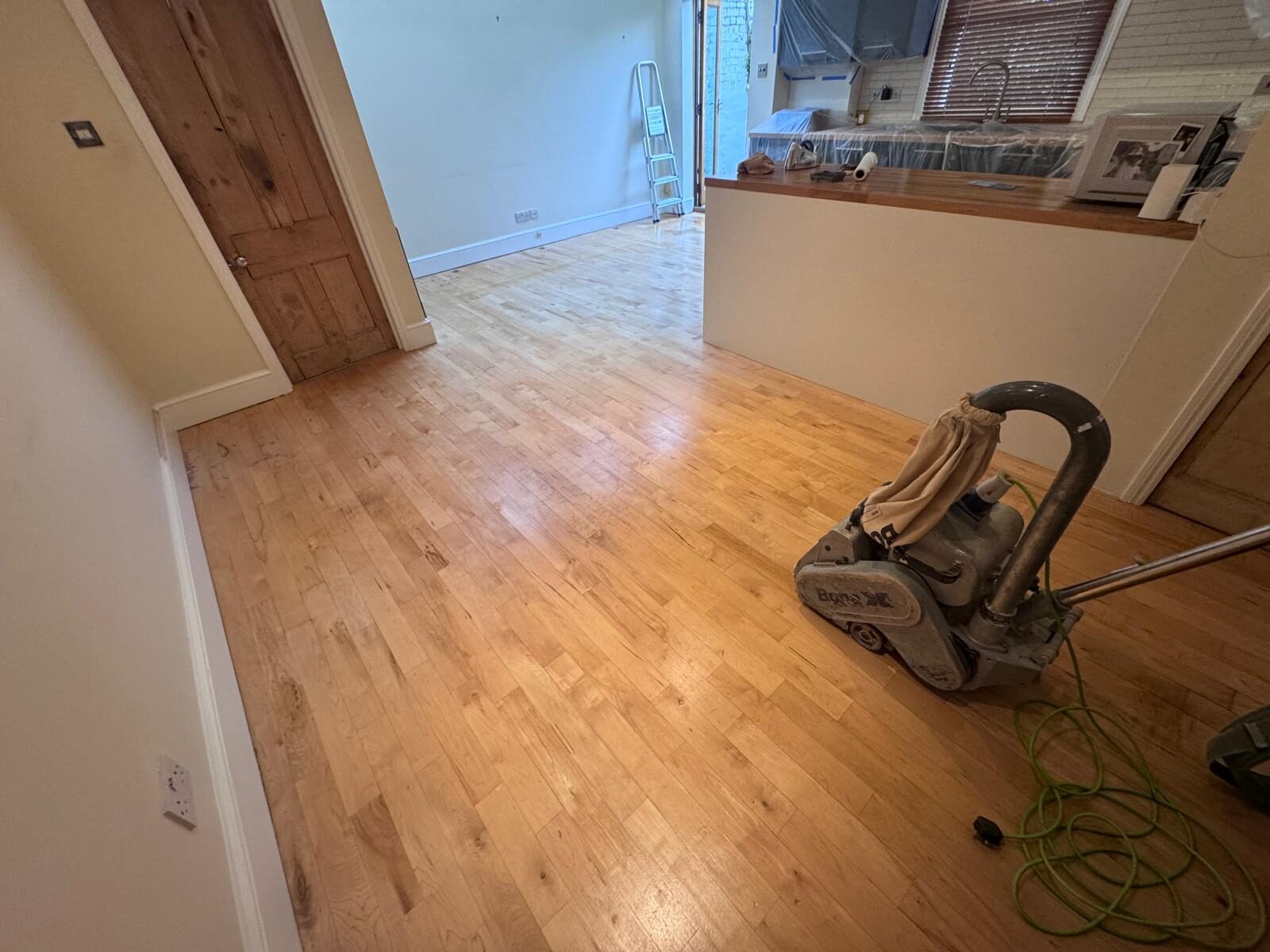 A professional Bona floor sander being used on a light solid maple strip hardwood floor to restore its natural beauty and character.