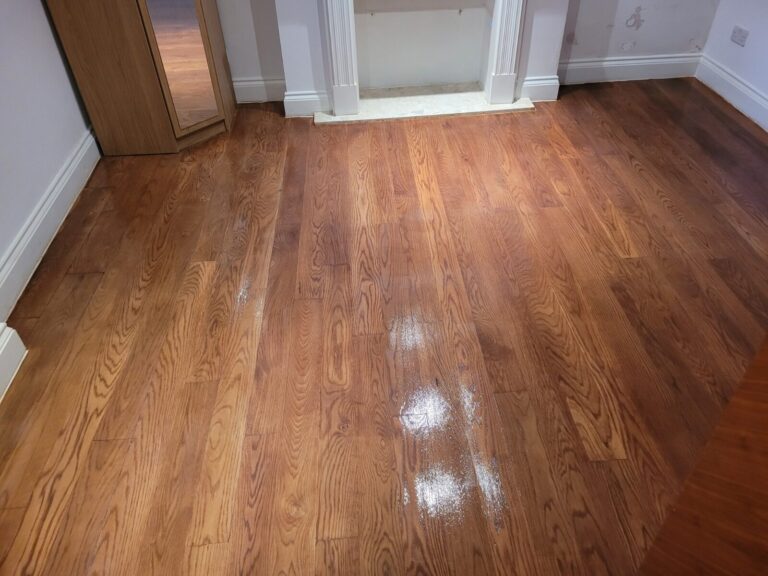 A beautifully restored solid white oak hardwood floor in a living room, featuring a rich warm stain and a polished semi-gloss finish.