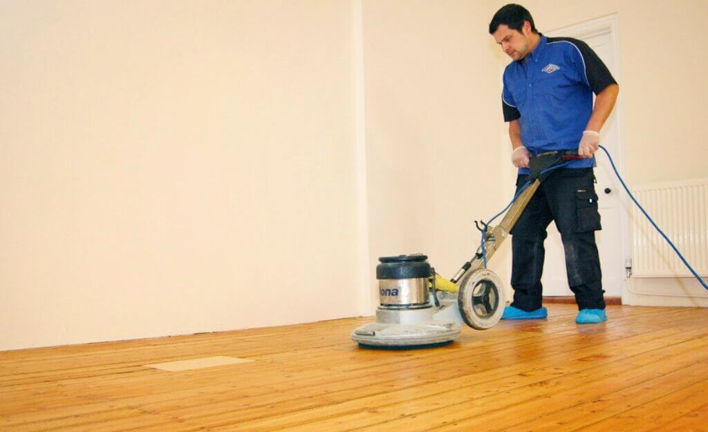 A professional from Mr. Sander® sands a parquet floor in a living area in the UK using a Bona FlexiSand 1.9 machine. The powerful Bona FlexiSand has a 1.9 kW motor, 230V voltage, 147 rpm abrasive disc speed, and a 407mm disc diameter, ensuring precise floor refinishing.
