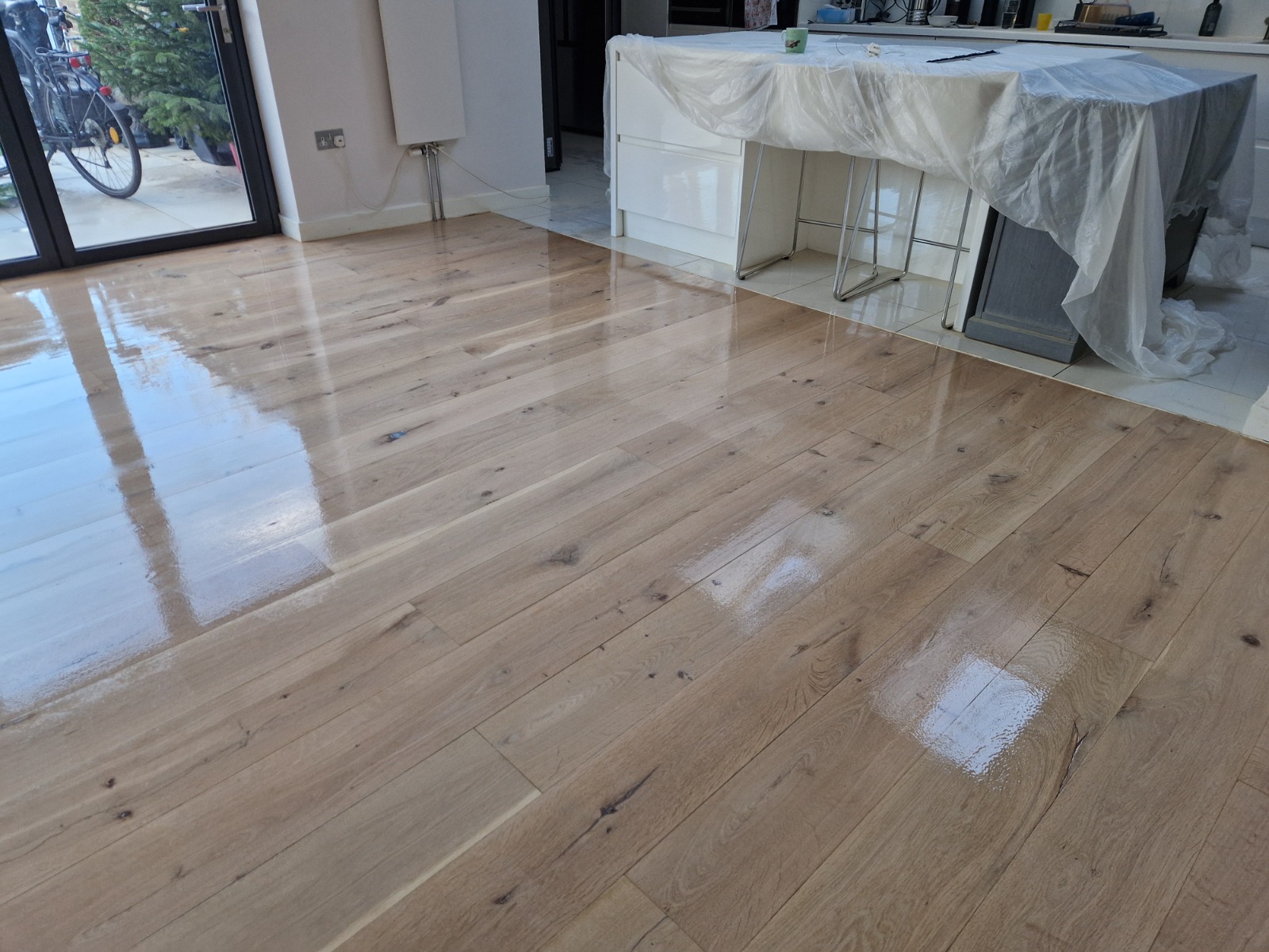 A wide-plank engineered oak kitchen floor showing a high-gloss reflective finish after a professional buffing and polishing service.