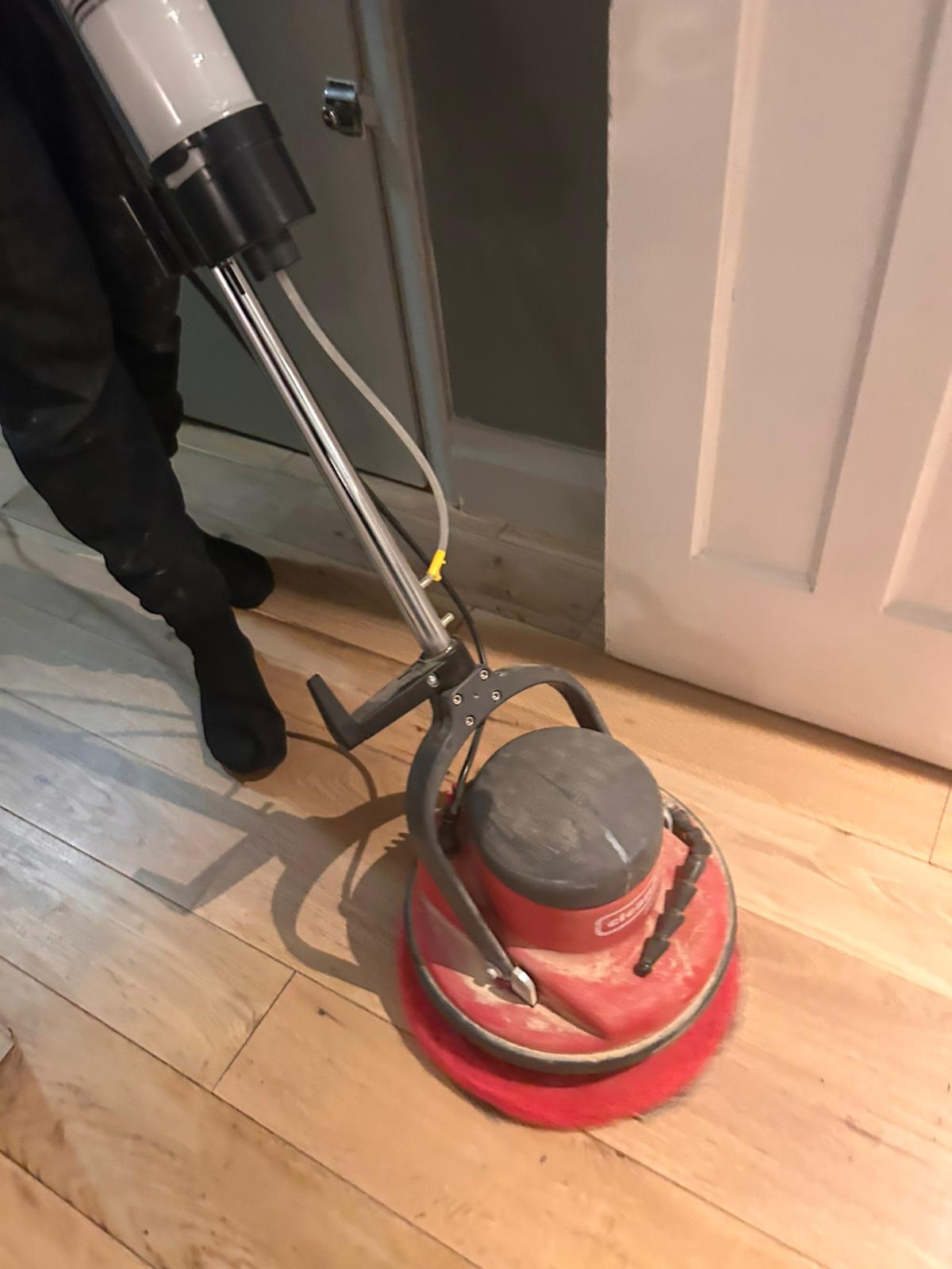 A professional floor technician using a rotary floor machine for the buffing and polishing of a light-toned engineered oak plank floor.
