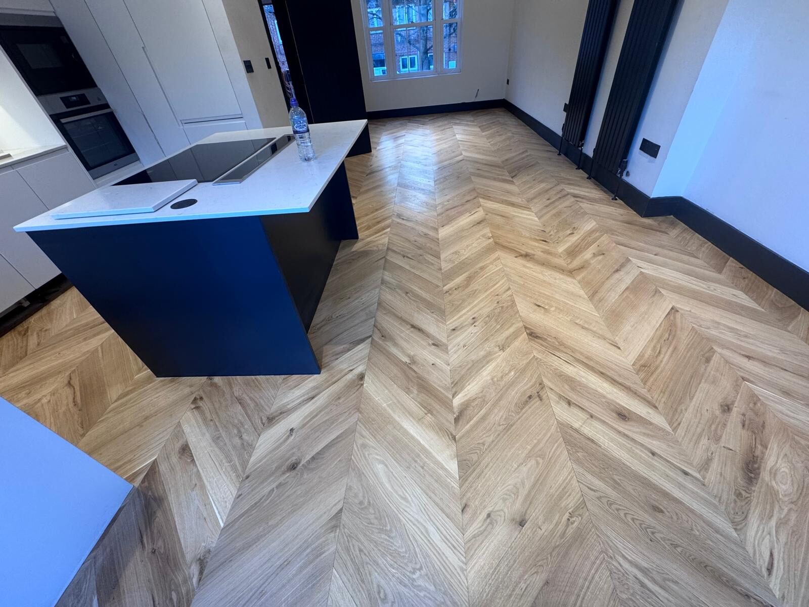 Chevron Parquet Sanding results on an oak chevron parquet wood floor in a modern kitchen, showing a smooth, even finish around a central island unit.
