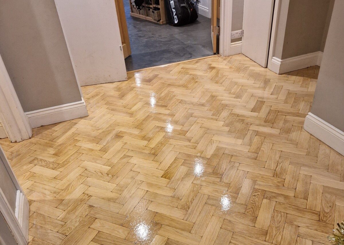 A freshly restored oak herringbone parquet floor showing the results of professional chevron parquet sanding with a high-gloss finish in a hallway.