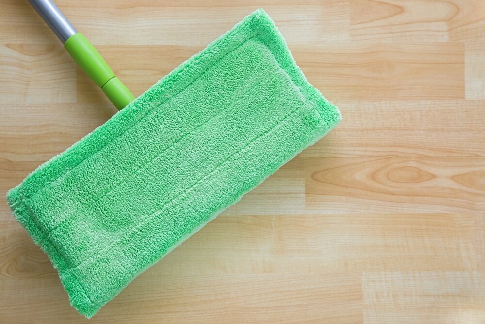 Close-up of a green microfiber mop head on a newly refinished wooden floor by Mr Sander®. The image highlights the importance of using soft, gentle cleaning tools to maintain the floor's shine and condition.
