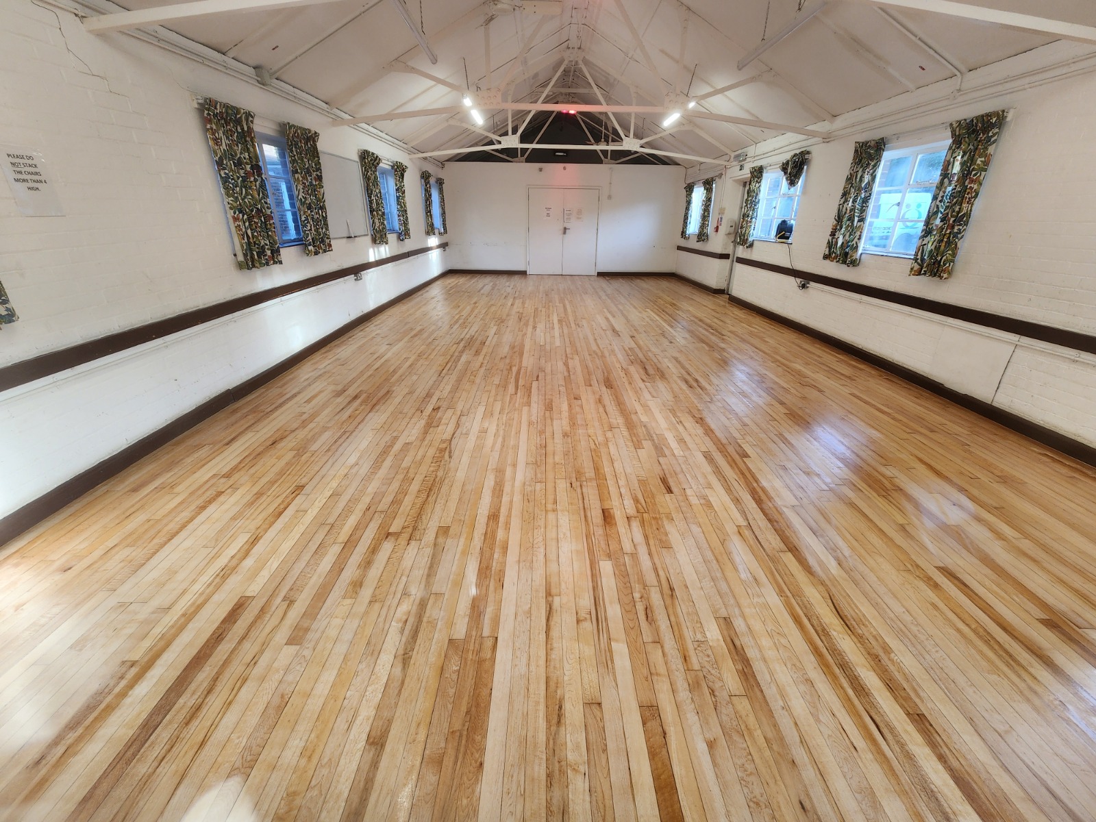 Commercial floor sanding completed on a hardwood strip floor, showing a smooth, polished timber surface inside a large commercial hall.