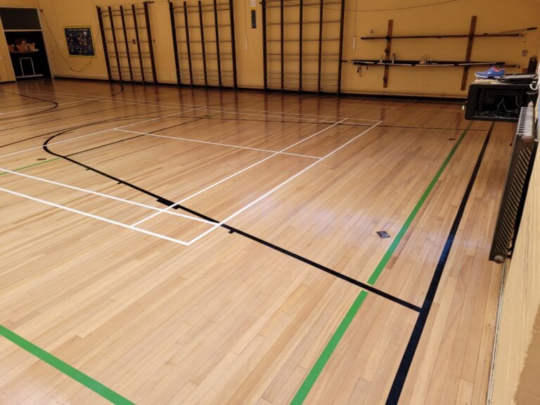Newly finished maple hardwood strip sports hall floor after Commercial Floor Sanding, with crisp black, white and green court lines on the polished surface.