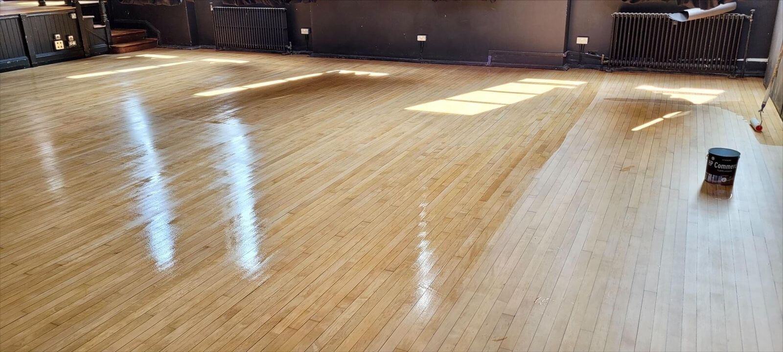 Community Hall Floor Sanding on a maple hardwood strip hall floor, showing fresh lacquer being applied to create a glossy, durable finish across the large wooden space.