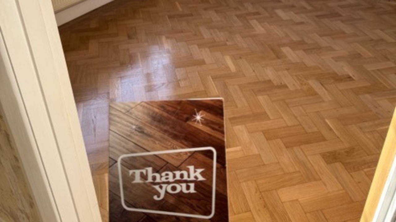 A freshly restored oak herringbone parquet floor with a light, natural finish and a "Thank You" card in the foreground.