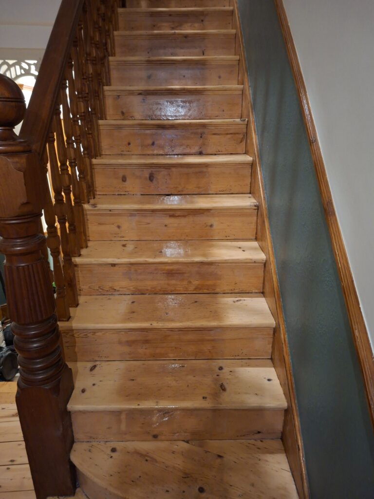 A completed Staircase Revival showcasing polished natural pine wood treads and risers with a clear protective finish and a traditional wooden banister.