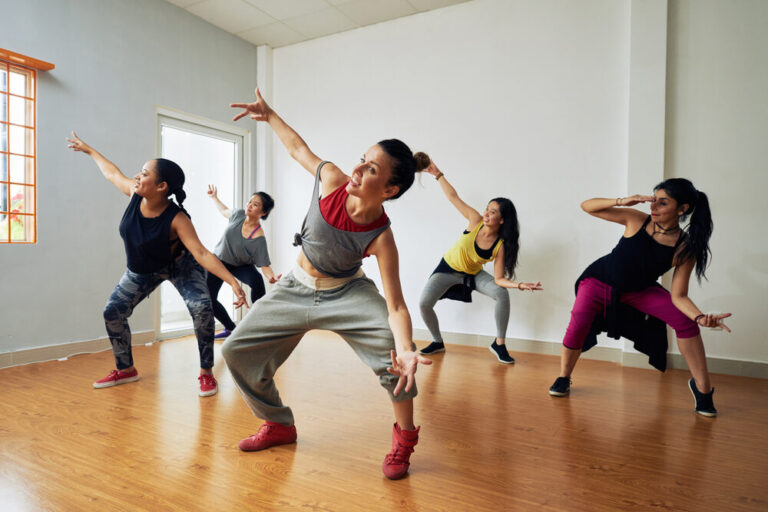 Five dancers practising an energetic routine on a sprung oak‑effect studio floor, demonstrating comfort, safety and bounce