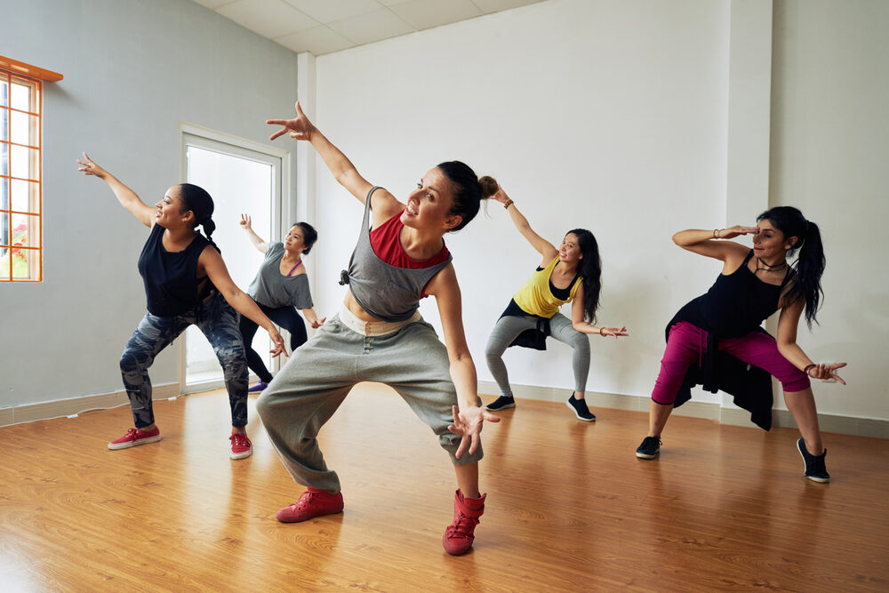 Five dancers practising an energetic routine on a sprung oak‑effect studio floor, demonstrating comfort, safety and bounce