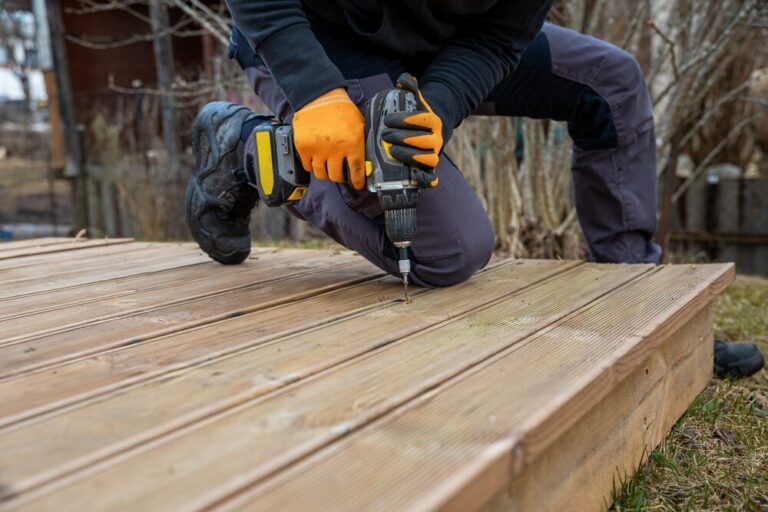 Mr Sander® technician kneeling outdoors, fastening pressure-treated pine decking boards with a cordless drill.