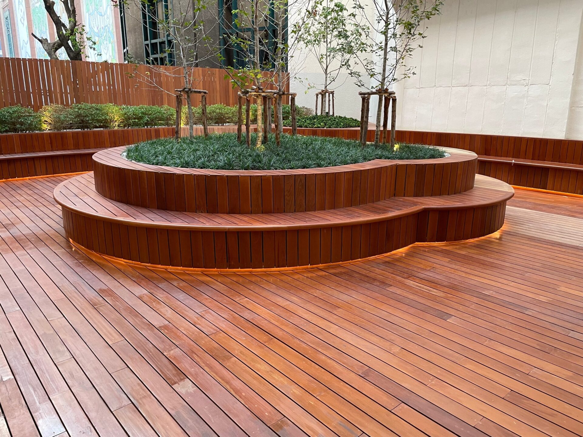 Beautifully finished hardwood timber decking floor after Deck Sanding, featuring curved timber seating and raised planters in an elegant courtyard.