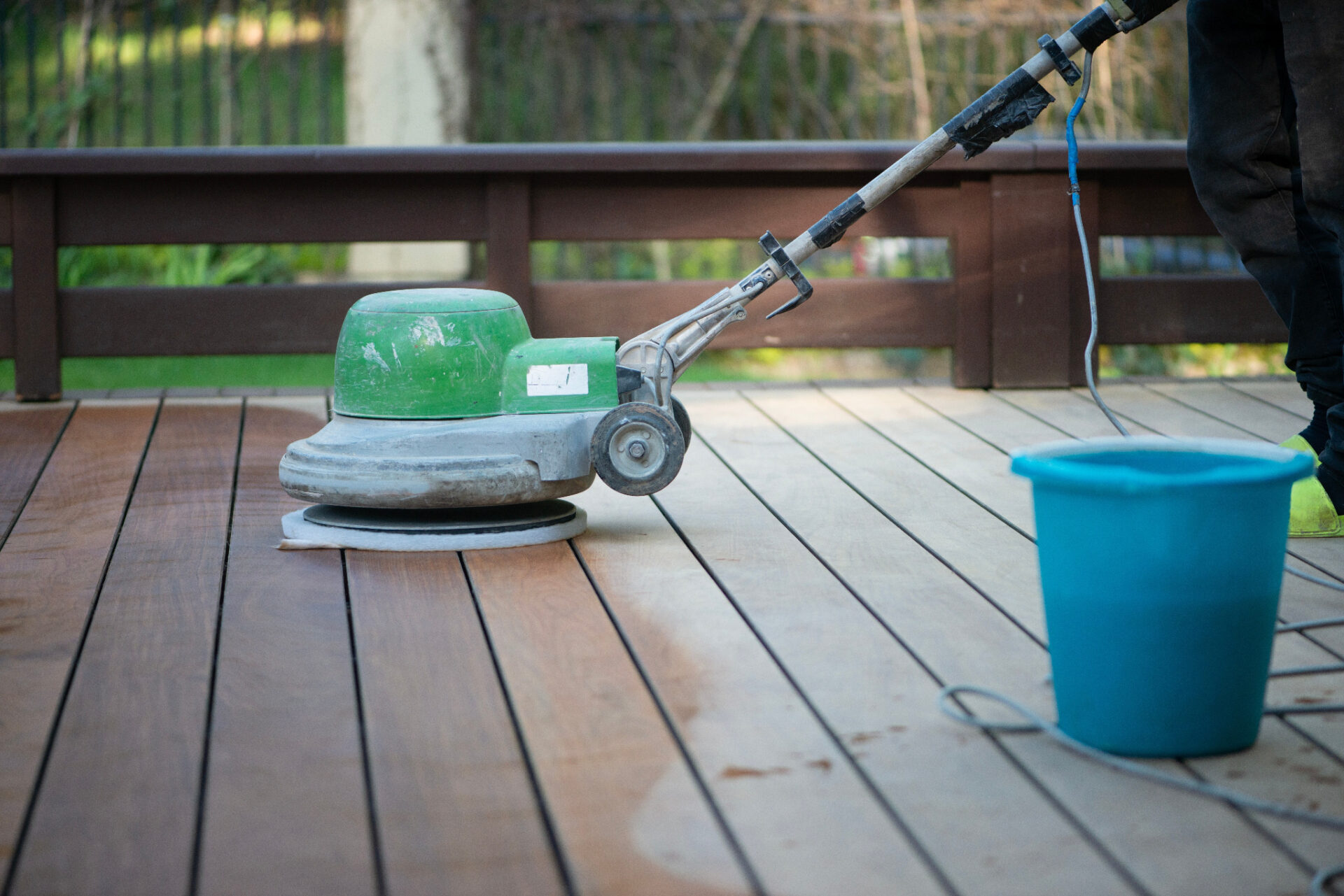 Deck Sanding in London with a green floor sander restoring a teak hardwood decking floor, smoothing the sun-faded timber boards ready for finishing.