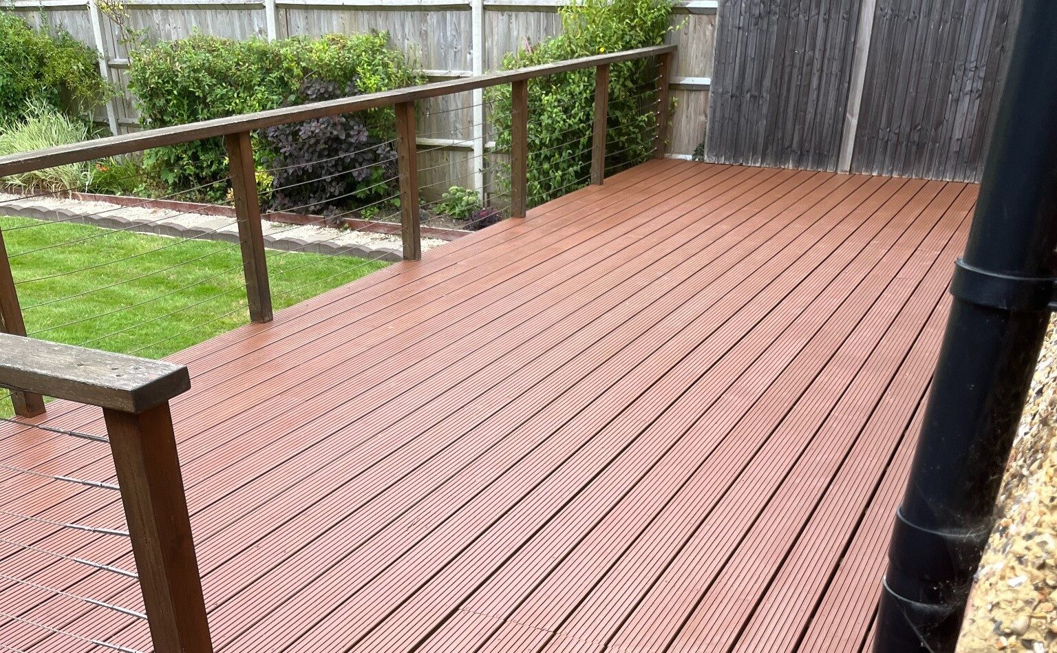 Large garden with grooved softwood timber decking floor finished in a warm terracotta tone, illustrating Deck Stain Colour Ideas for modern outdoor spaces.