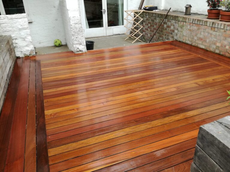 Freshly stained hardwood timber garden deck showcasing Deck Stain Colour Ideas with rich brown and amber tones on smooth wooden floor boards.