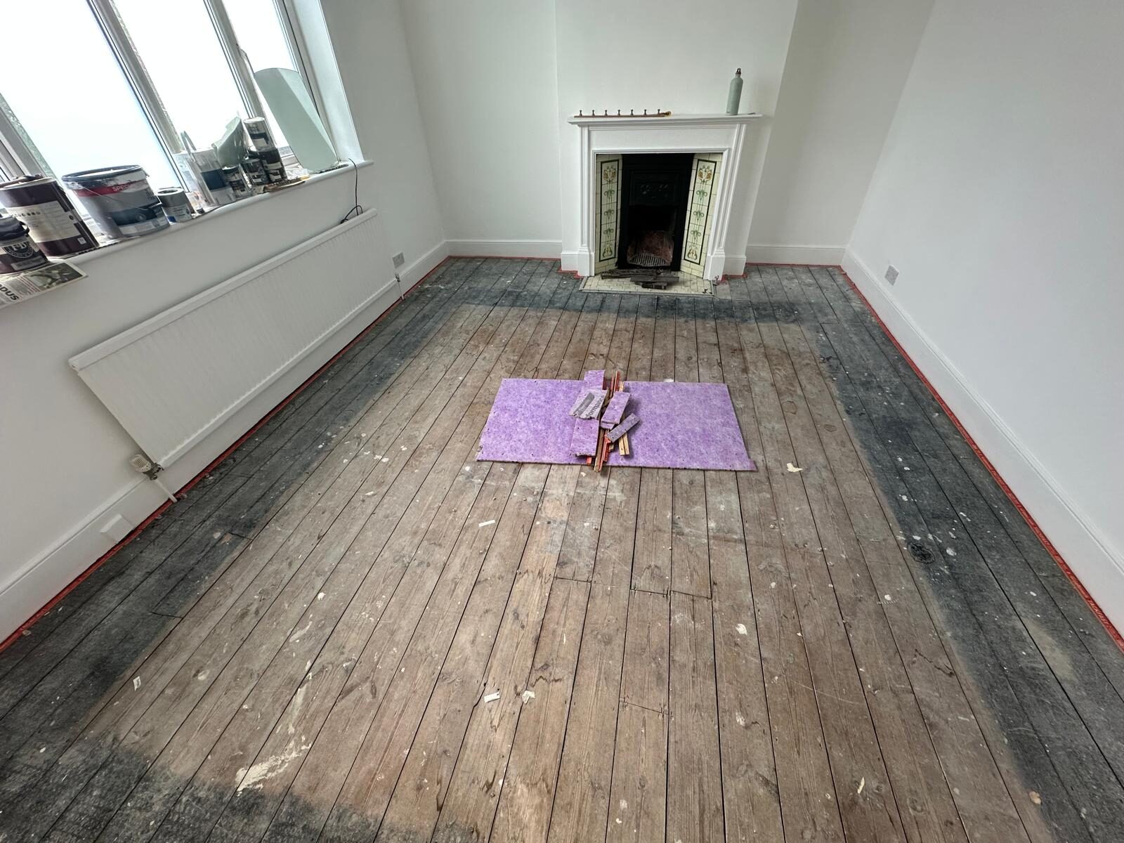 DIY Sanding Floorboards — worn pine boards before sanding, room prepped with taped skirtings and tools laid out near a period fireplace