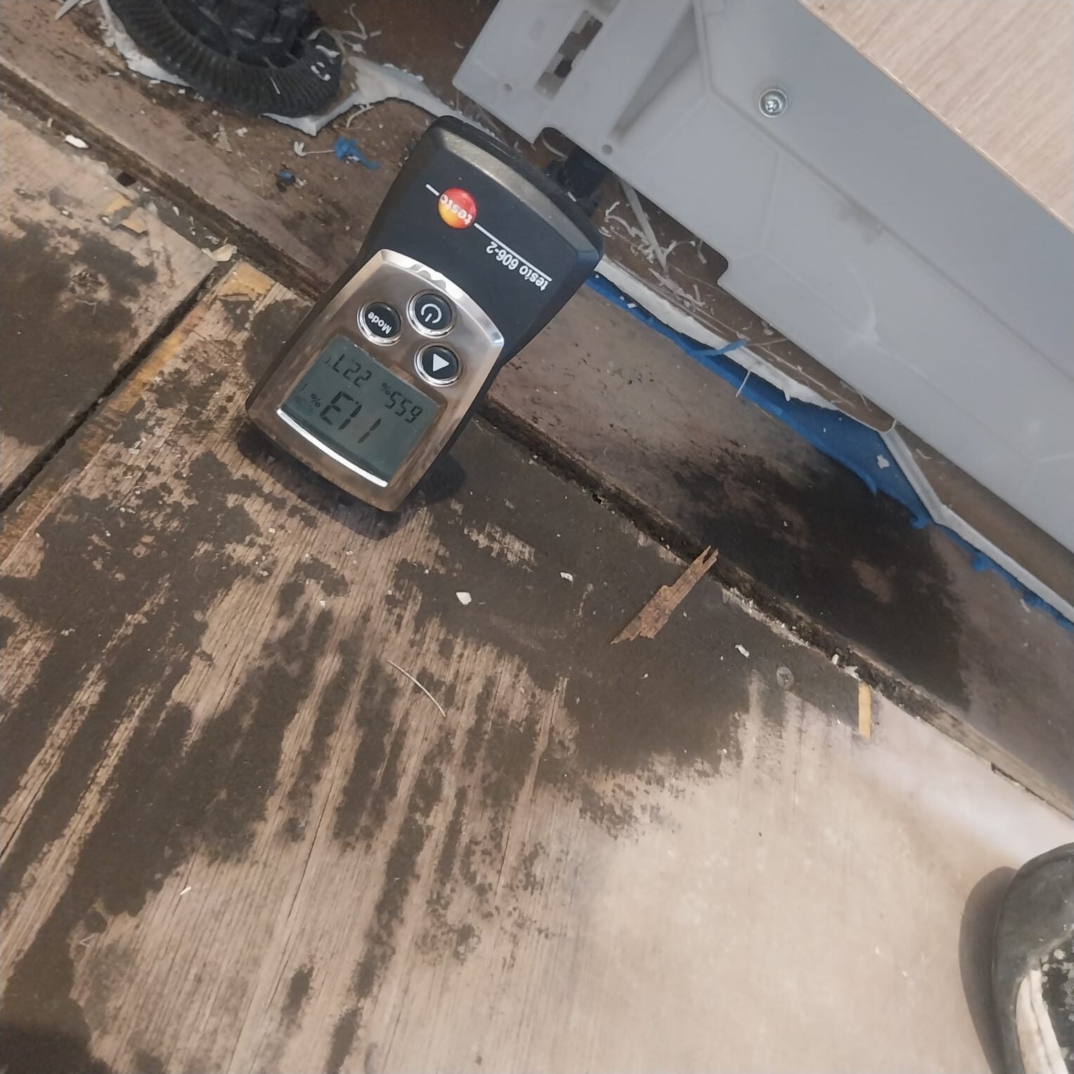 Moisture meter on a water-stained engineered oak parquet wood floor, highlighting the warning: Donot Fit Over a Wet Screed before refitting.