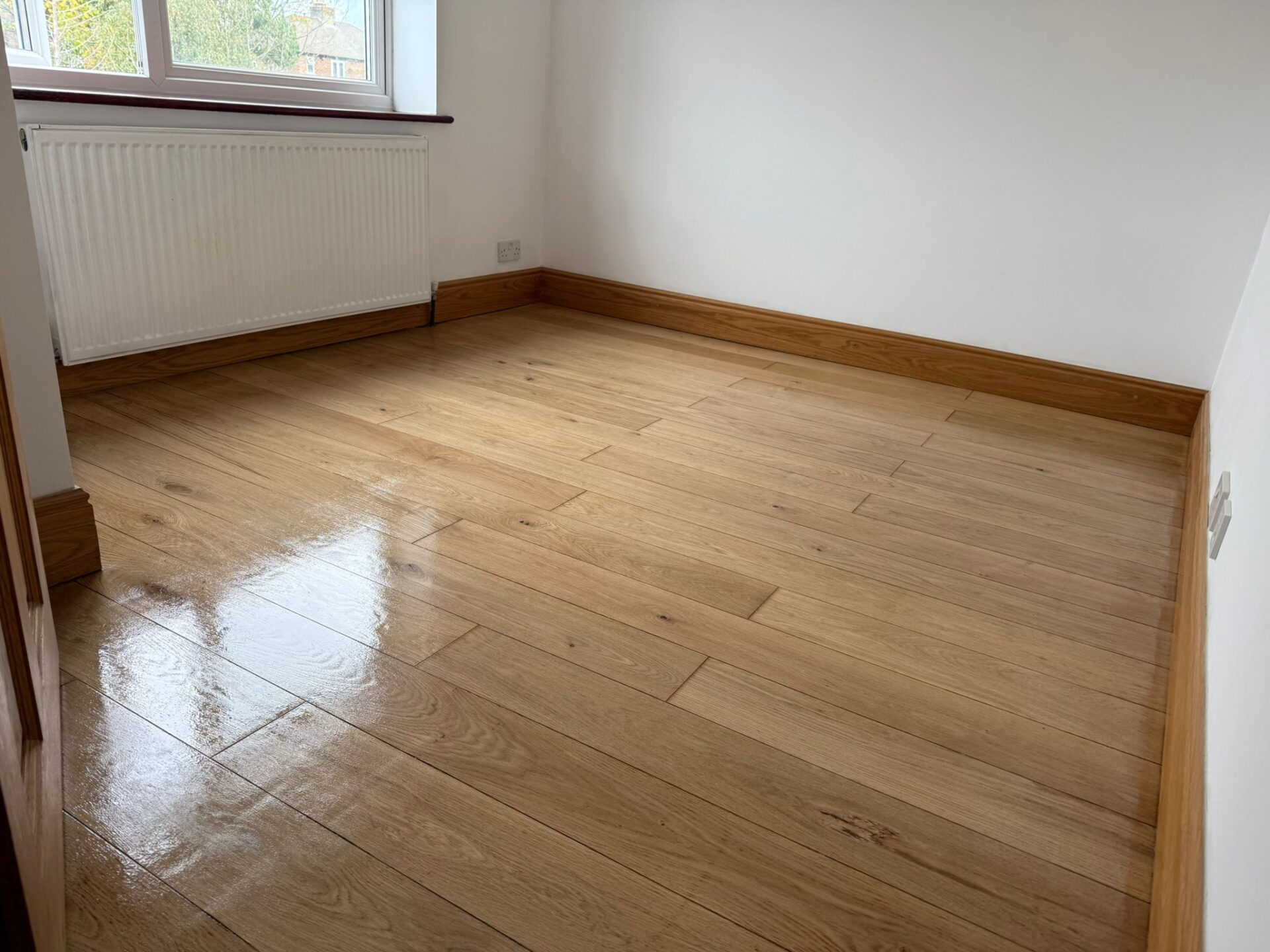 Finished oak engineered plank wood floor with visible sheen near the window—reminder: Donot Fit Over a Wet Screed to avoid moisture-related defects.