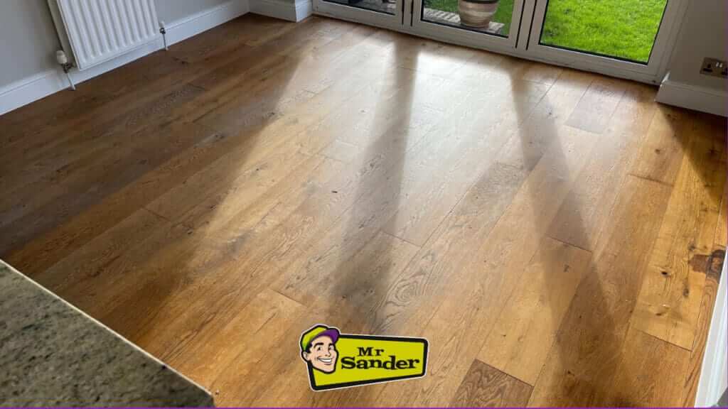 A newly sanded and refinished hardwood floor with sunlight streaming through a window.