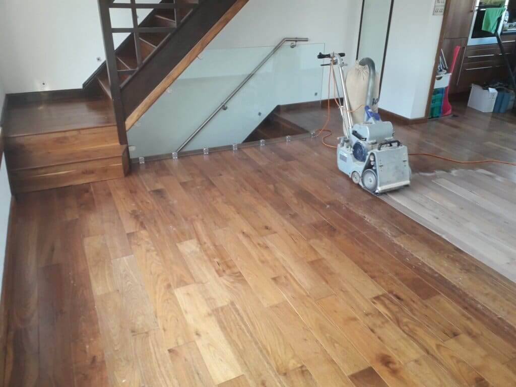 A professional from Mr Sander® is sanding a solid oak hardwood in a living room in, UK using a Bona Belt sander (AMO110000.3). The machine features a 2.2 kW motor, 230 V voltage, 50 Hz frequency, and a sanding belt size of 200 x 750 mm or 250 x 750 mm. The total weight is 74 kg.