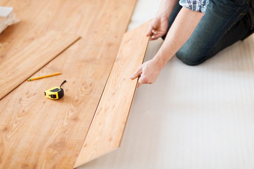 Home fitter aligning a click-lock oak engineered wood plank over underlay, demonstrating Engineered Click vs Tongue and Groove installation approaches on an oak engineered floor.