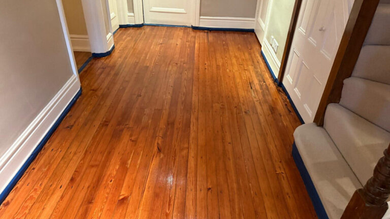 A polished oak engineered floor in a hallway showing the results of an engineered floor edge repair along the skirting boards.