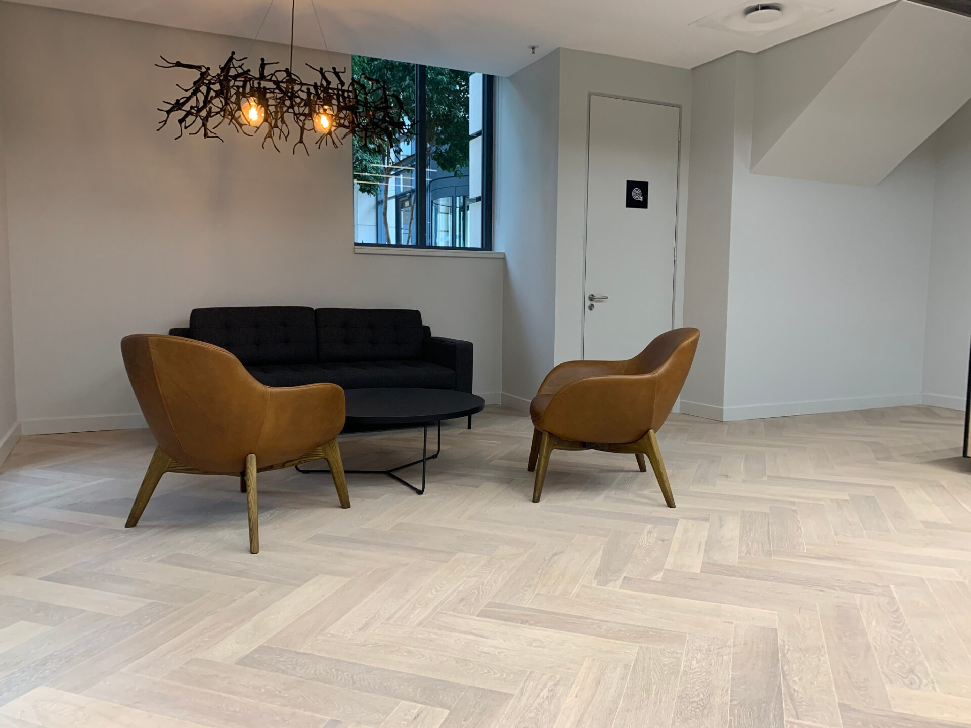 Modern lounge with pale oak Engineered Herringbone flooring, armchairs and sofa, showing clean, luxury finish.