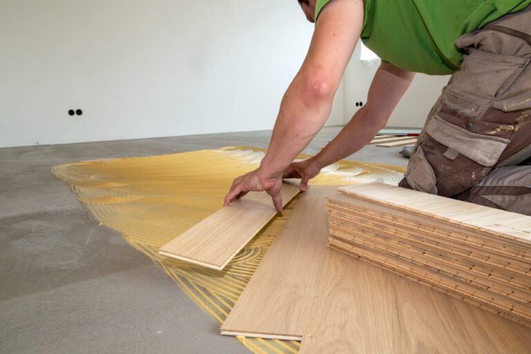 A professional from Mr Sander® installing engineered oak wood flooring during a Floor Installation for Commercial Spaces project, carefully placing planks on adhesive over a concrete subfloor.