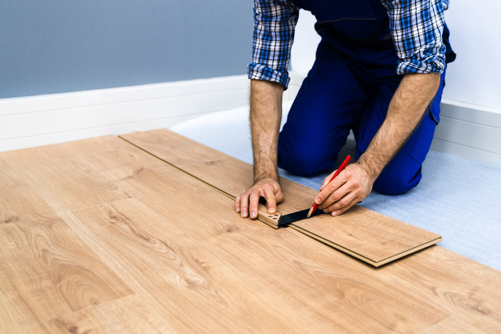 Installer marking an oak engineered wood floor plank for precise cutting, preparing a low-tog build-up for Engineered Over Underfloor Heating installation.