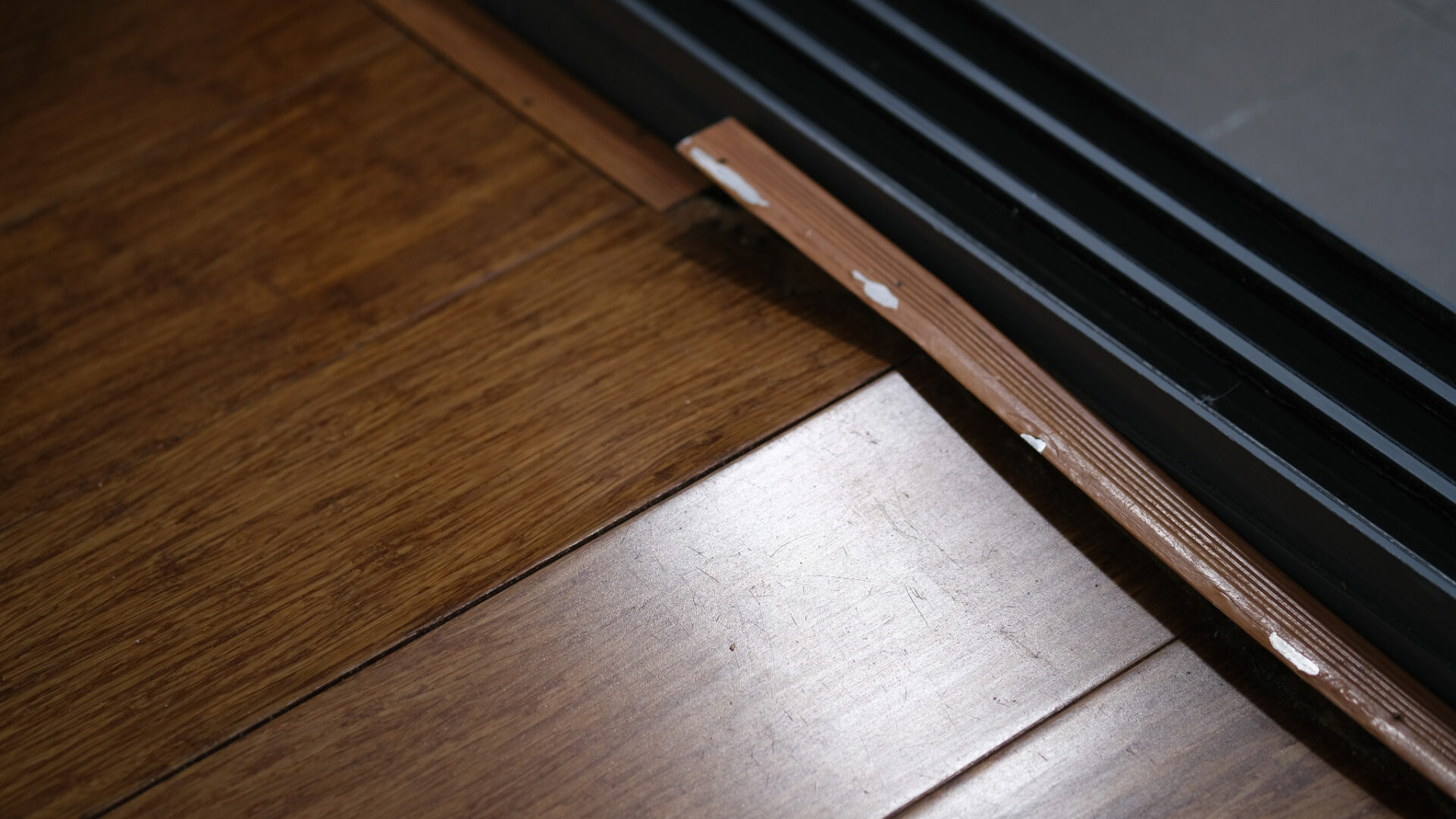 Engineered Wood Floor Repair at a doorway showing damaged threshold strip and scratched engineered oak wood floor planks ready for professional fixing.