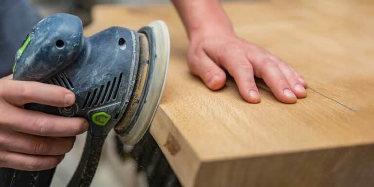 A close-up of a hand holding a piece of sandpaper and sanding a wooden surface.