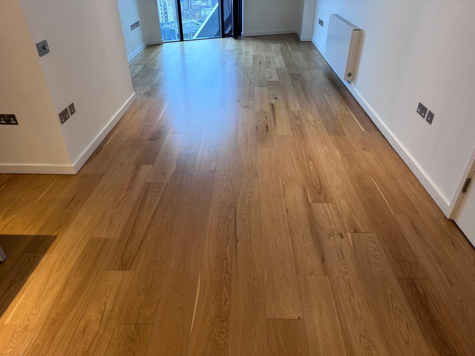 A wide-angle view of a professionally finished natural oak hardwood plank floor in a modern, bright apartment.