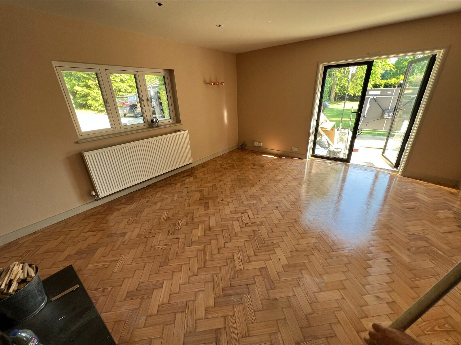 A wide-angle view of a living room featuring a glossy, restored oak herringbone parquet floor after professional sanding and sealing.