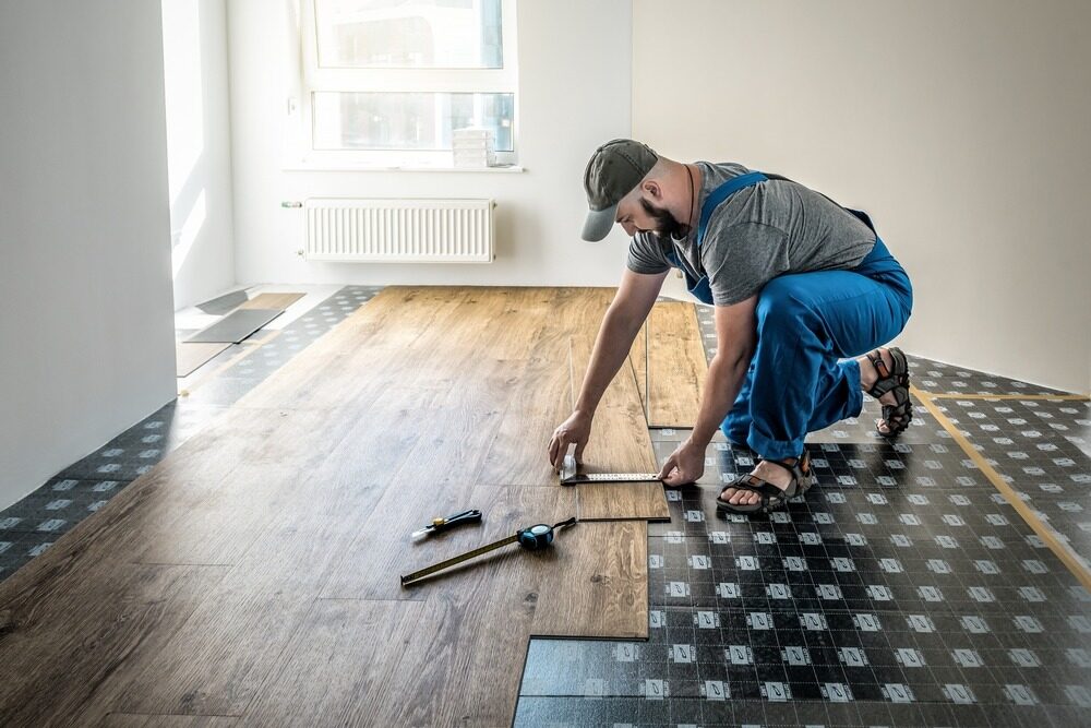 Worker fitting wood floors with precision tools, installing oak laminate flooring over prepared subfloor.