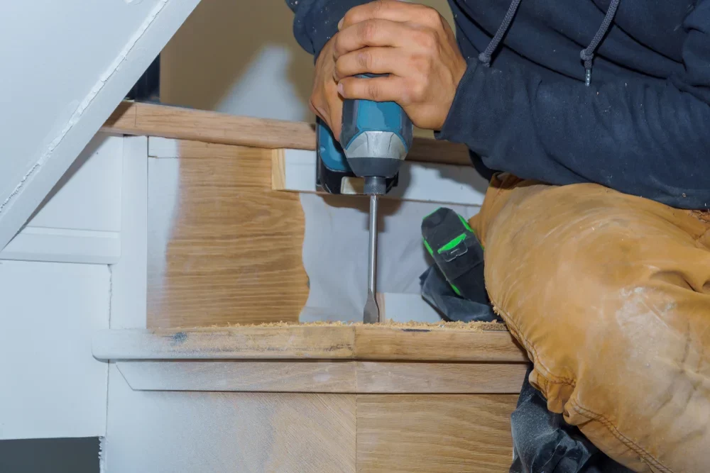 Fixing Noisy Stairs with a professional using a drill to secure oak hardwood stair treads on a timber staircase, reducing movement and creaks in the wooden floor.