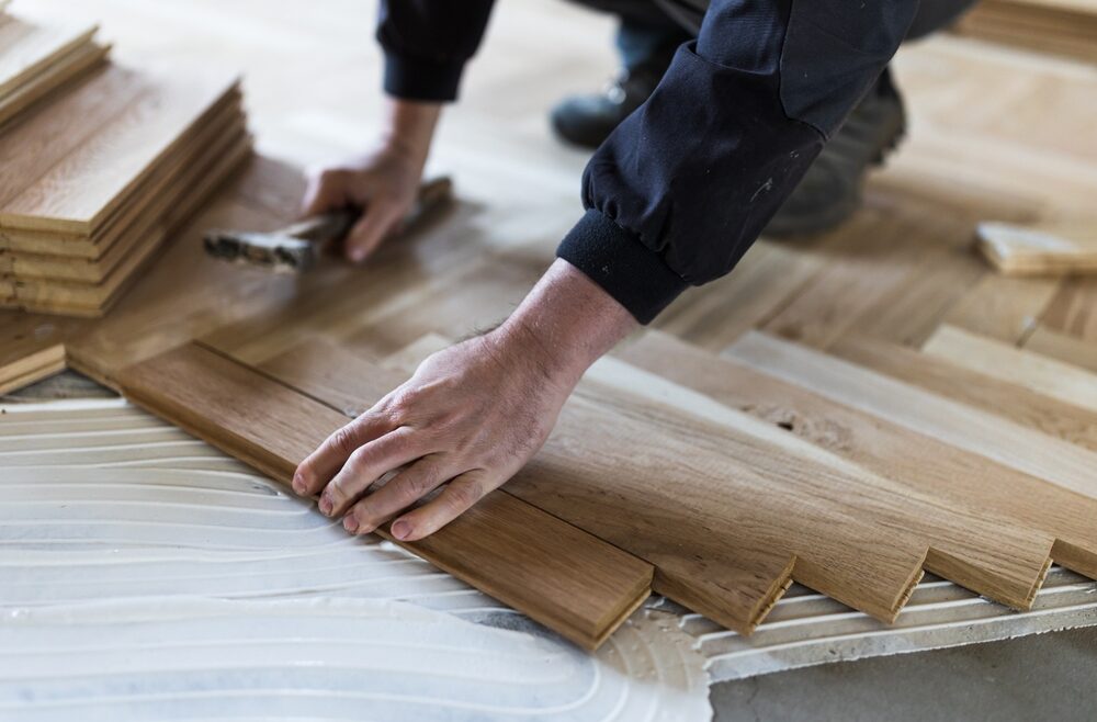 Hands of a floor fitter positioning an oak herringbone parquet border into adhesive—detail of Floor Installation for Listed Buildings.