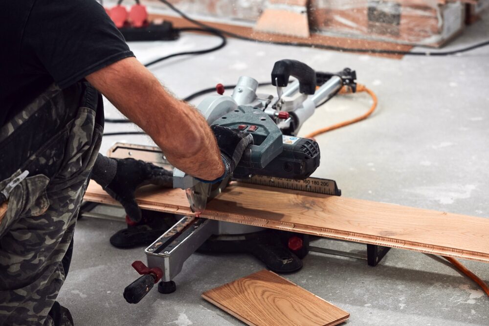 Installer cutting an engineered oak floorboard with a sliding mitre saw, demonstrating precise detailing for Floor Installation for Listed Buildings.