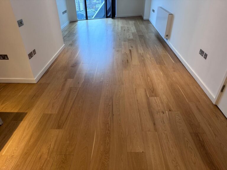 A wide-angle view of a beautifully finished oak hardwood plank floor in an empty modern room, showcasing floor makeovers that wow with a natural satin sheen.