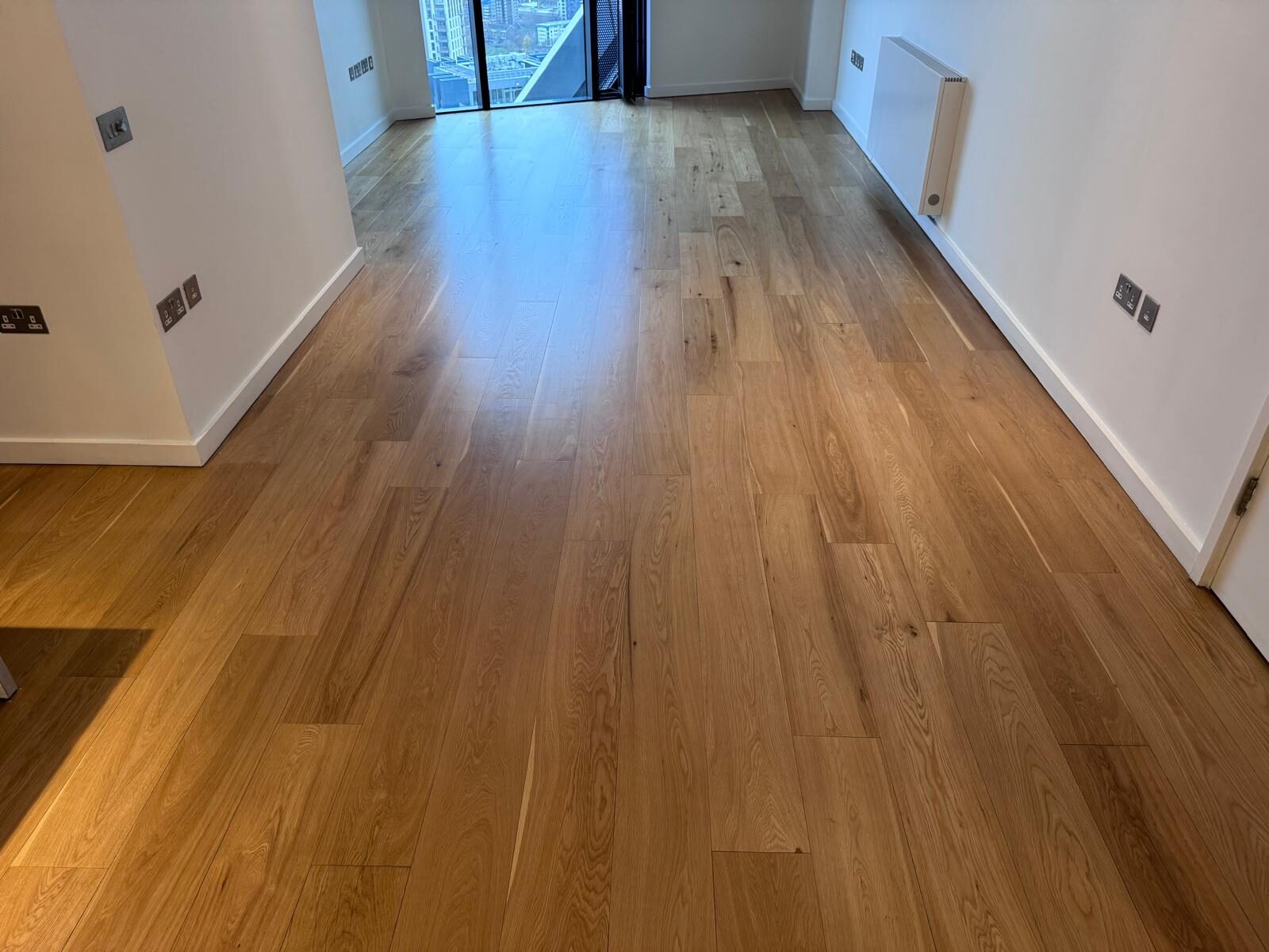 A wide-angle view of a beautifully finished oak hardwood plank floor in an empty modern room, showcasing floor makeovers that wow with a natural satin sheen.