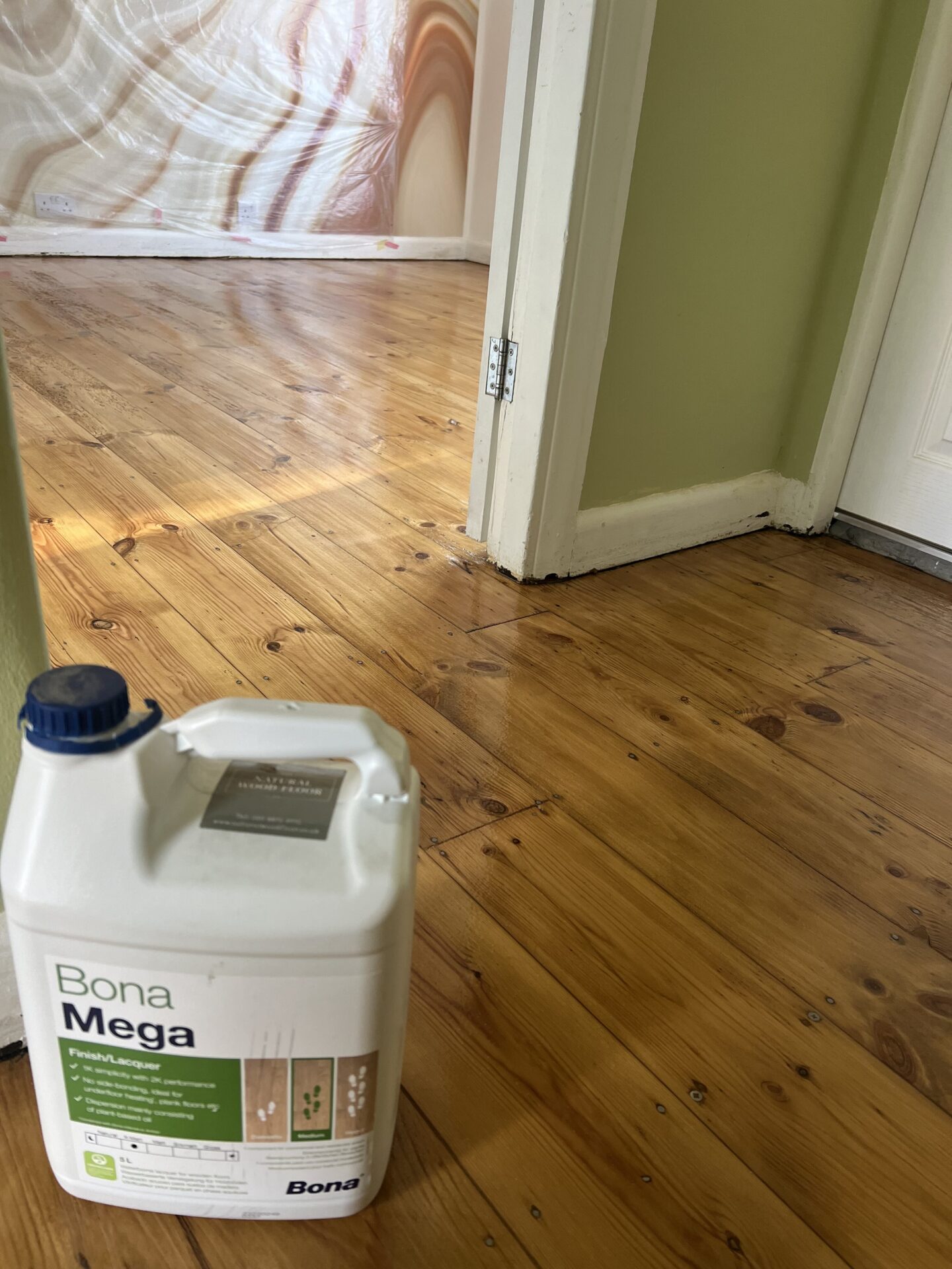 Bona Mega lacquer container on a newly sanded and lacquered pine floor during Floor Sanding in Historic Homes in West London, with plastic-screened walls in the background.