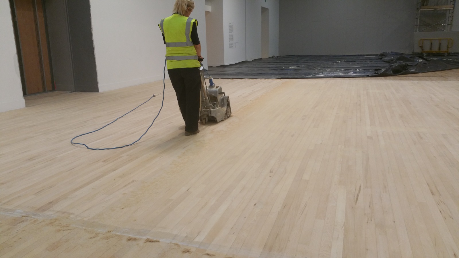 Floor Sanding in London on a maple hardwood strip sports hall floor, with a professional technician using an industrial sanding machine to refinish the surface.