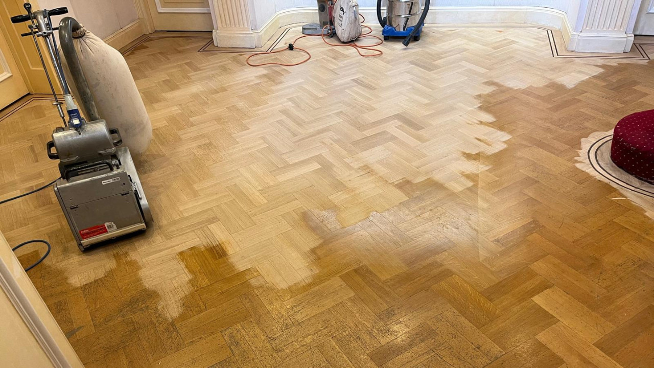 Professional Floor Sanding in London in progress on an oak herringbone parquet floor, with sanding machines showing the contrast between old finish and freshly sanded wood.