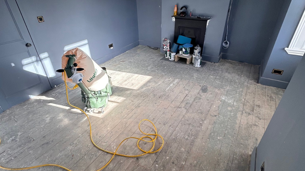 Floor Sanding in London on pine softwood floorboards, showing a living room prepared for sanding with a professional drum sander positioned on the worn wood floor.