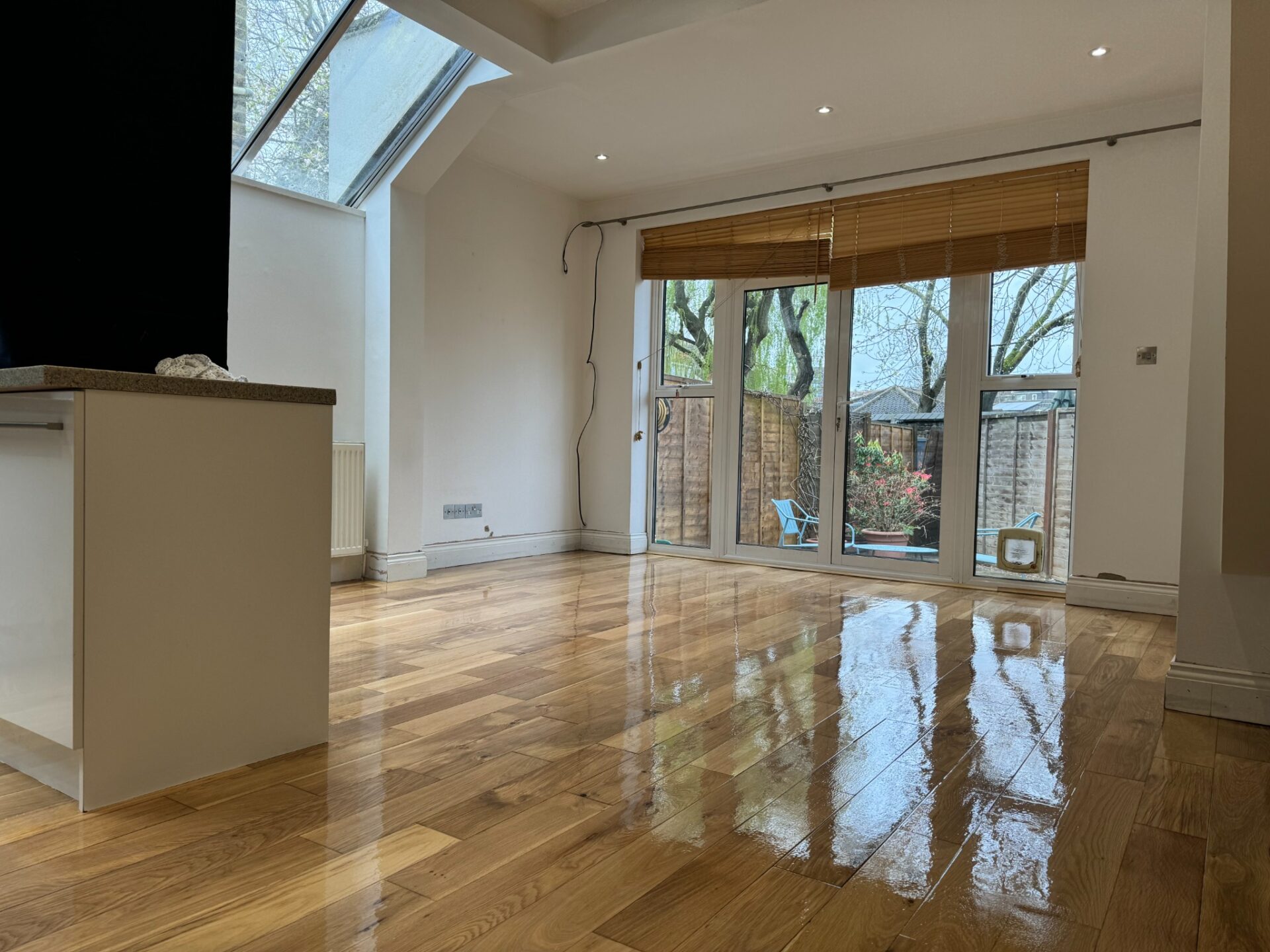 Open-plan kitchen–diner with skylight and garden doors showing oak floorboards professionally sanded and refinished to a clear gloss lacquer, reflecting natural light.