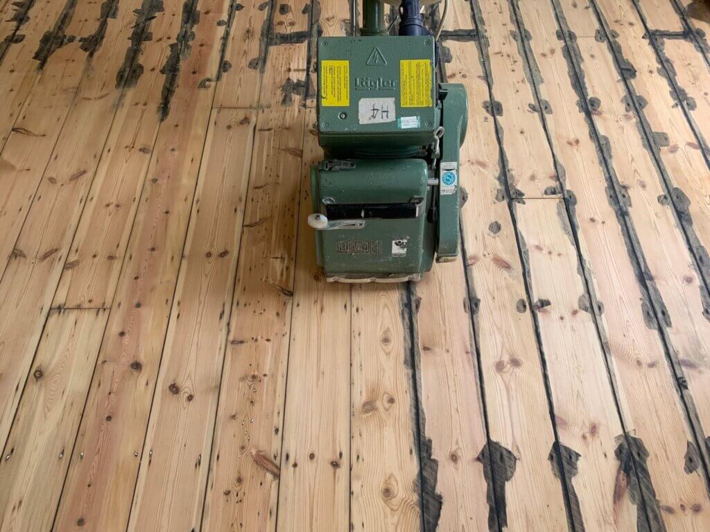 A man from Mr Sander® is sanding a parquet floor in a living area in the UK using a Lagler HUMMEL® floor sanding machine. The HUMMEL® features LED work lighting, a 230V motor, 2.2 kW power, and a 200 mm drum width, ensuring high-quality, dust-free sanding.