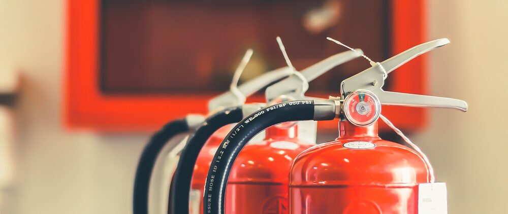 Row of red fire extinguishers in a workshop, illustrating Floor Sanding Safety—be ready for sparks, solvents and oil-soaked rags during refinishing.