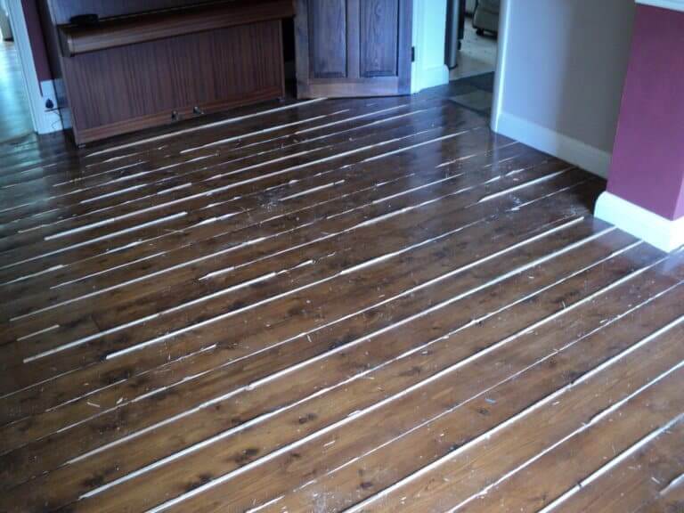 A dark-stained wooden floor with visible gaps and wear, ready for restoration through sanding and refinishing.
