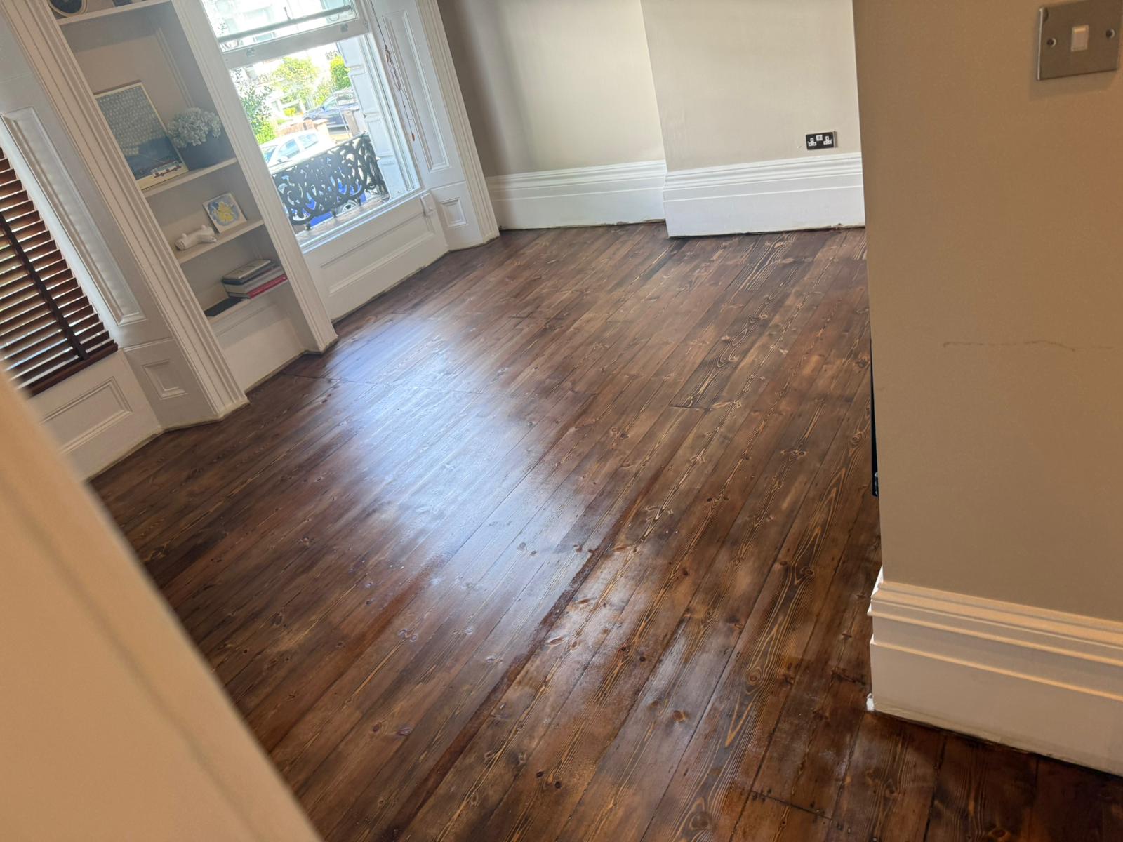 A high-angle view of Victorian pine softwood floorboards finished with dark wood floor staining and a reflective gloss topcoat.