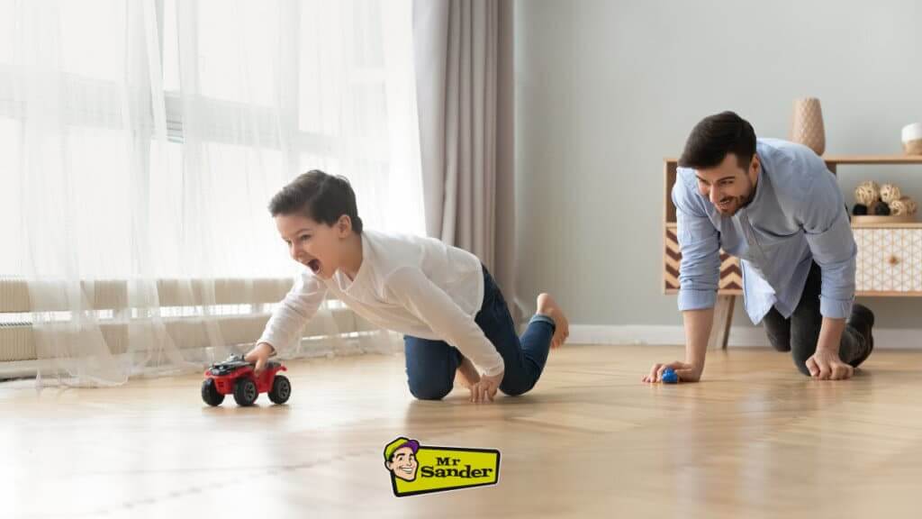 A father and son playing with toy cars on a beautifully refinished herringbone-patterned oak floor by Mr Sander® in a bright and cheerful living room.